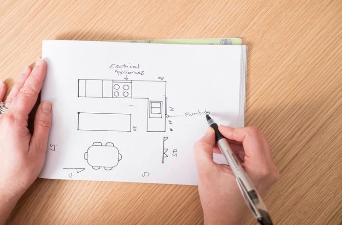 A person sketches a kitchen layout, highlighting the need to finalise plans, measurements, and renovation timelines before work begins.