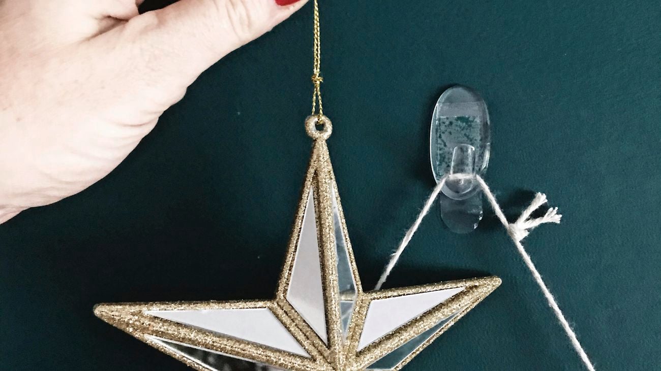 Hand hanging a silver and gold star ornament on a hook attached to a dark green wall