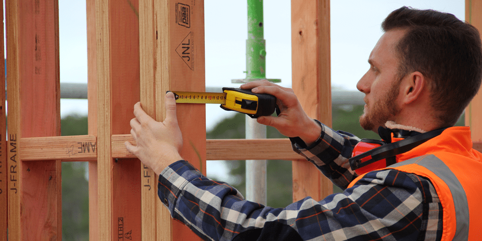 A builder measuring framing timber at a construction site