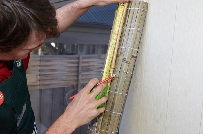 A person measuring a rolled up bamboo blind
