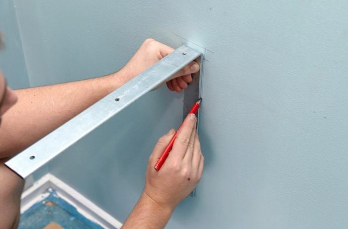 A person marking the position for an angle bracket on a wall