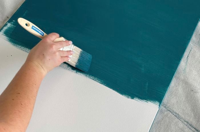 A bold, blue paint being applied on a canvas with a paint brush