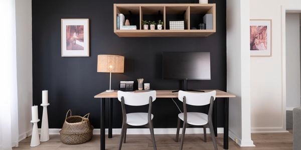 Study with black feature wall, timber desk, computer screen and lamp.