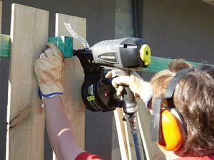 Person wearing ear protection attaching fence palings using a nail gun