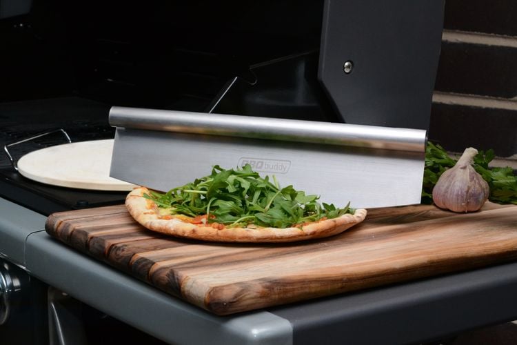 Pizza sitting on wooden chopping board next to barbecue