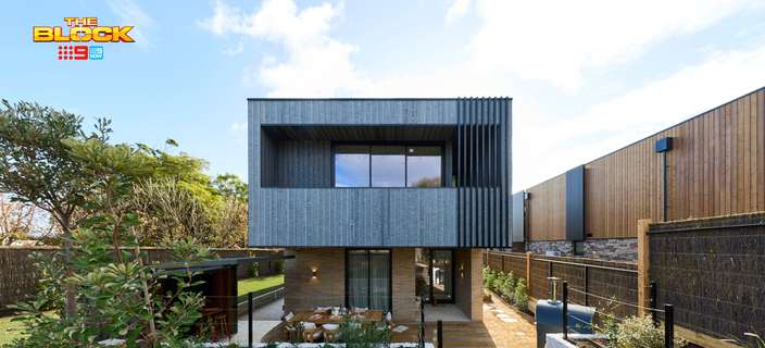 Modern two-storey home featuring dark vertical cladding, large windows, a timber walkway and landscaped garden beds.