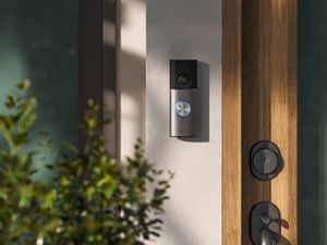 Smart video doorbell mounted beside a front door with camera lens and illuminated ring button.