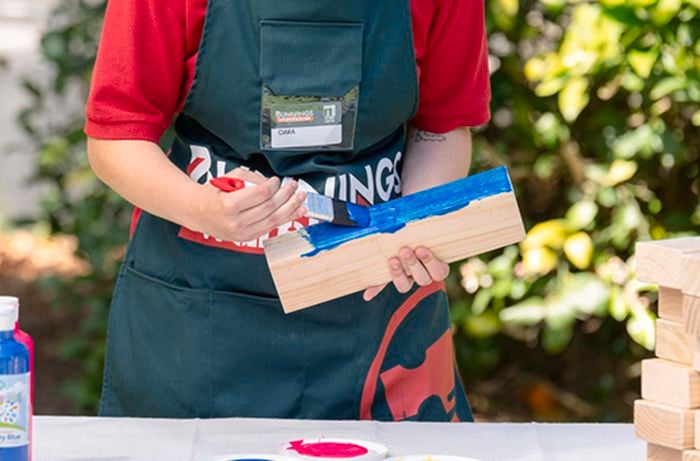 Bunnings team member painting a piece of timber with blue paint