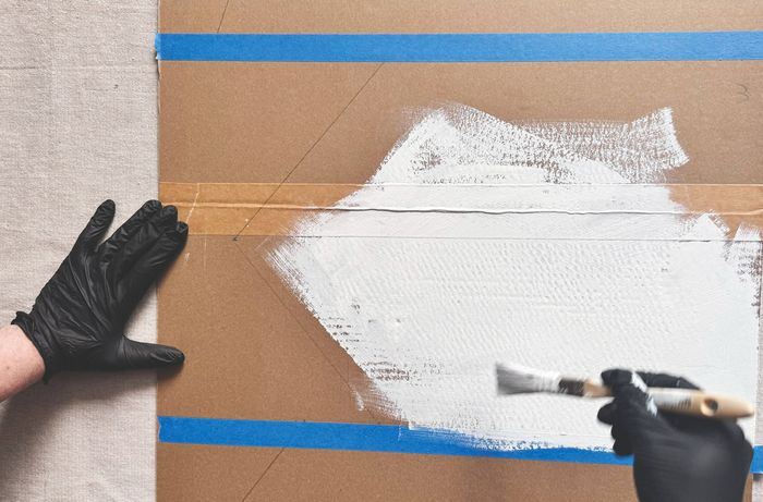 Hands using a metal ruler and a utility knife to cut a cardboard Advent calendar design.