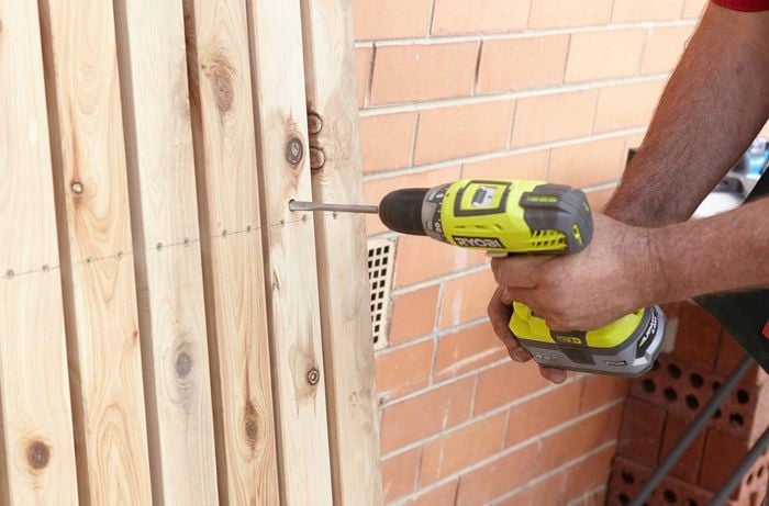 Person drilling a hole in a picket gate for a latch