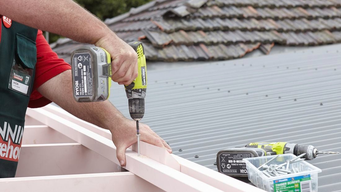 Person screwing shade batten into pergola roof.
