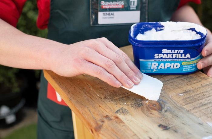 Person filling holes in timber with filler using a plastic applicator