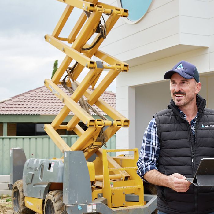 Trade professional holding a tablet beside a scissor lift at a residential construction site.