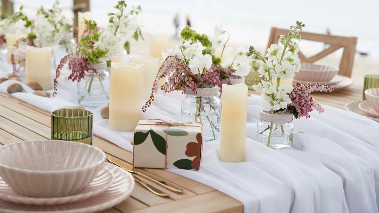 Present wrapped in cream patterned paper sitting on a dining table decorated with candles and flowers.
