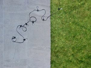 Lawn with pathway on side with a string of light bulbs.