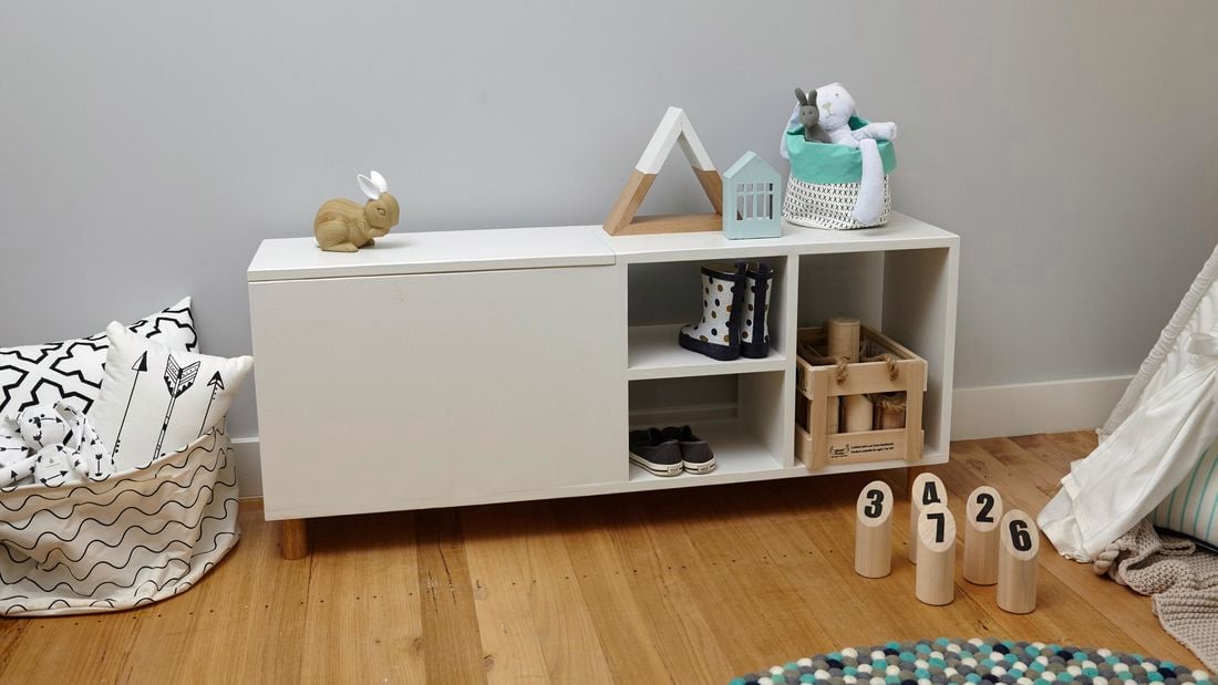 A completed wooden storage bench for children, holding shoes, boots, a toy crate, a toy rabbit and more