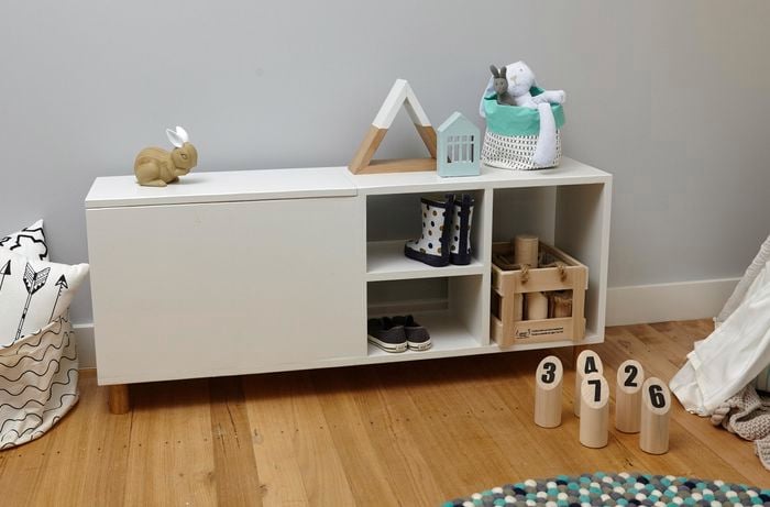A completed wooden storage bench for children, holding shoes, boots, a toy crate, a toy rabbit and more