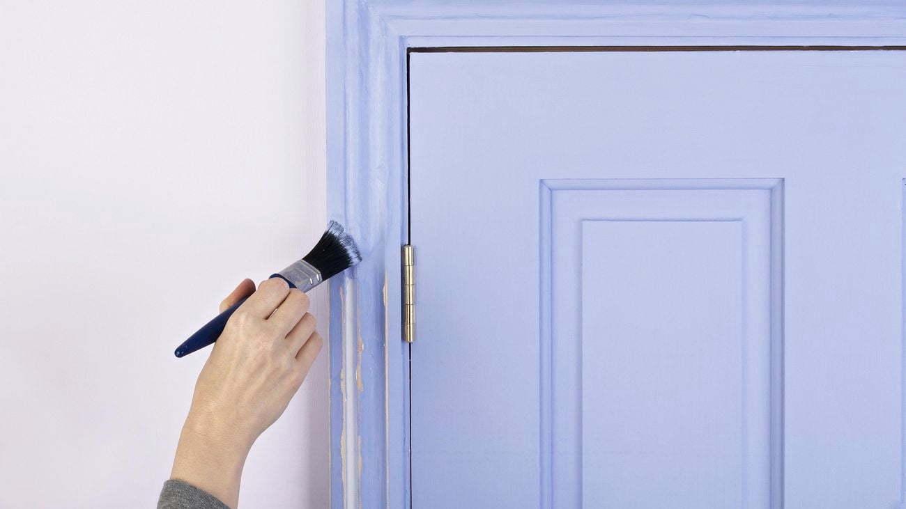 A hand painting the upper corner of a door frame blue with a paintbrush