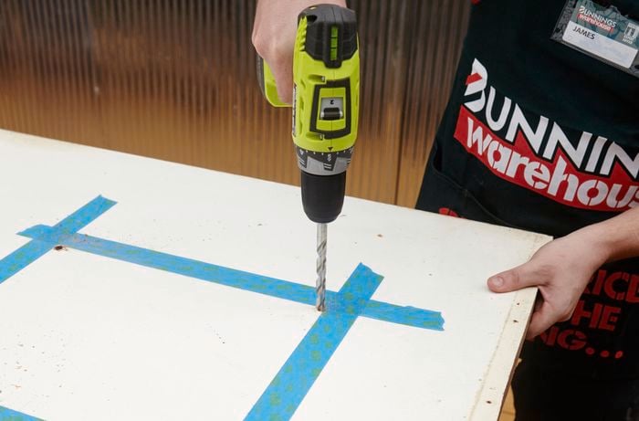 A person drilling holes in a door marked with masking tape