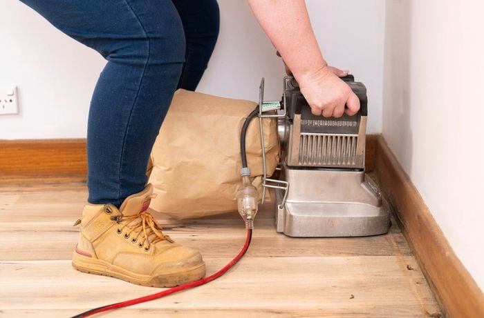 A close-up of a person using edging sander along the wall edge to create a smooth, even timber floor finish.
