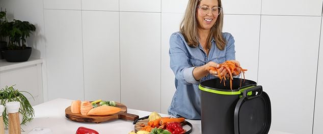 Person placing vegetable food scraps in a small bin for compost