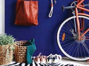 A blue pegboard wall with a shelf, bike, hat, keys and bag hanging up on it.