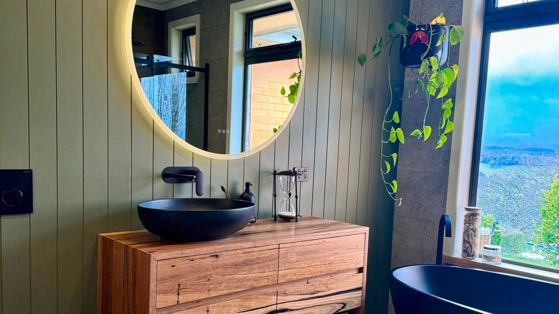 Renovated bathroom with black round basin, black tapeware, round mirror hanging on wall.