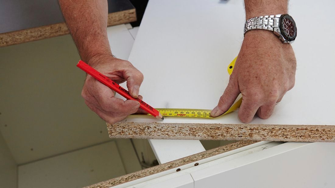 A tape measure and pencil being used to mark a piece of particle board