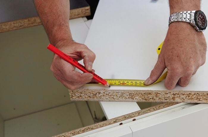 A tape measure and pencil being used to mark a piece of particle board