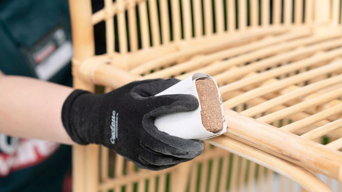 Person wearing safety gloves while sanding the wicker chair with sandpaper and sanding block.