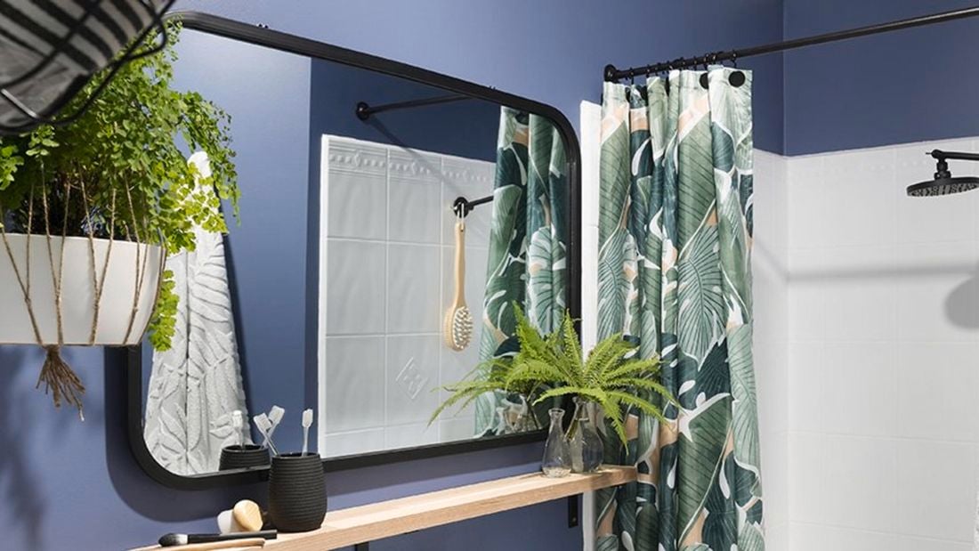 A bathroom with a curved edge mirror, hanging plant and colourful show curtain