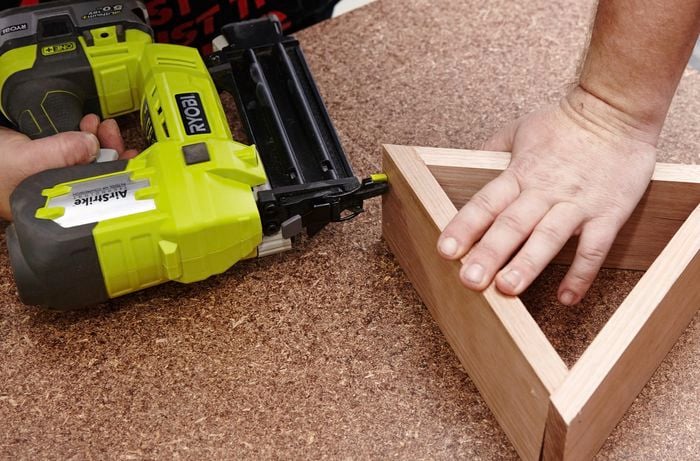 A person attaching three pieces of timber to form a triangle using a nail gun