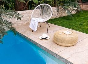 Outdoor lounge chair, hat and book next to edge of swimming pool in backyard with tropical plants