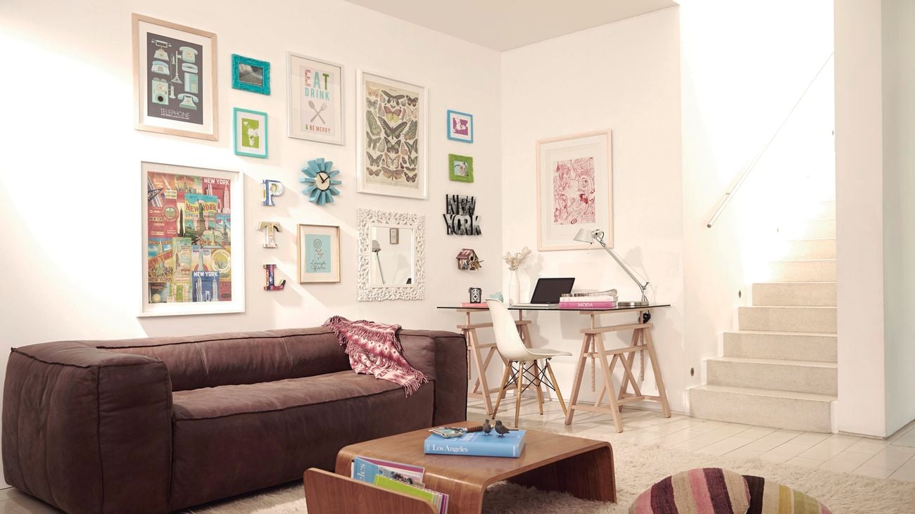 A lounge room with pictures hanging on the wall, a couch, a coffee table and a dining table in it.