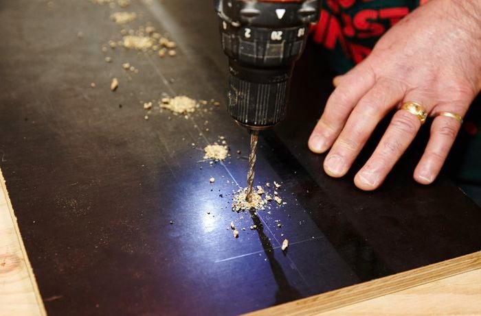 A person drilling holes in a sheet of plywood