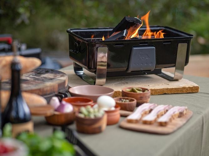 Portable BBQ with fire and coal and food prepped in small bowels with a chopping board.