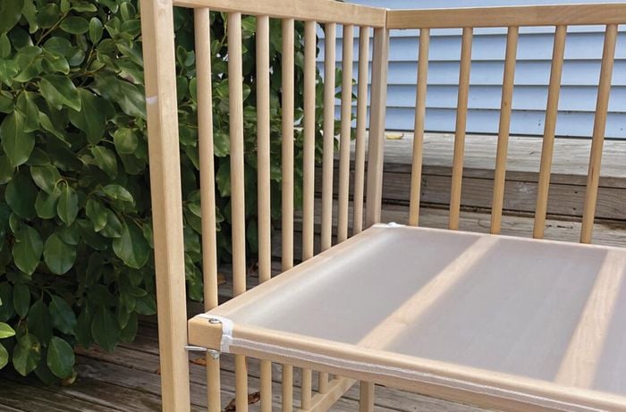 Left side of a wooden cot railings on a deck with an outdoor background