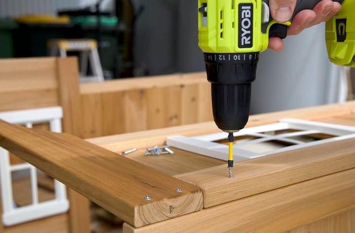 A hand holding a drill, drilling a screw into a piece of wood