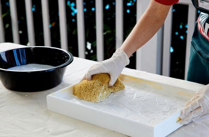 A woman removes excess grout from a tray using a damp cloth
