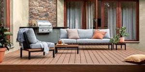 A Barbecue and outdoor setting on a timber decking with a cushion and pot plants on it.