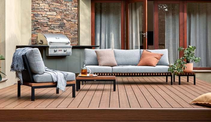 A Barbecue and outdoor setting on a timber decking with a cushion and pot plants on it.