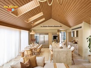 Open-plan kitchen and dining space from The Block, featuring a vaulted timber ceiling, marble island with bar stools, large fridge, neutral-toned dining area, and floor-to-ceiling curtains.