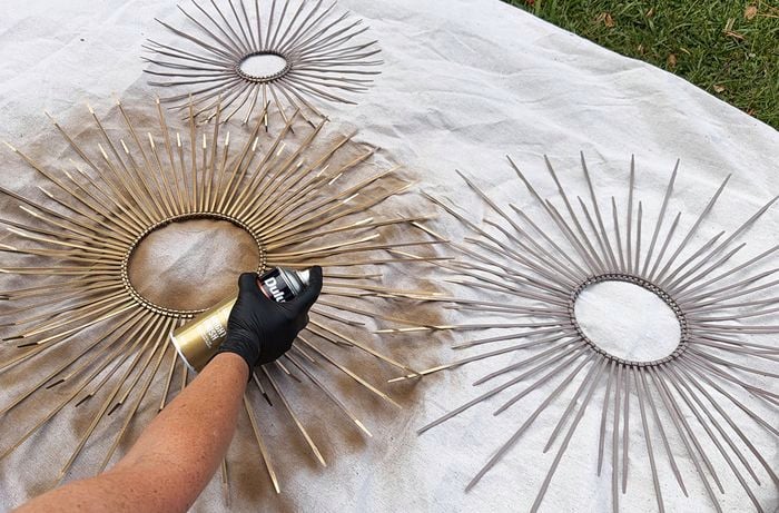 Three finished circular designs made from cable ties arranged in sunburst patterns, with one being spray-painted gold while the others remain grey, all laid out on a covered outdoor surface.