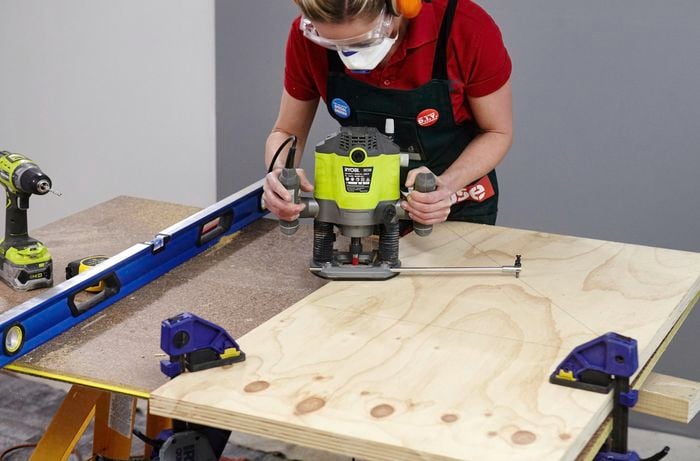 A person cutting a circle in plywood using a router