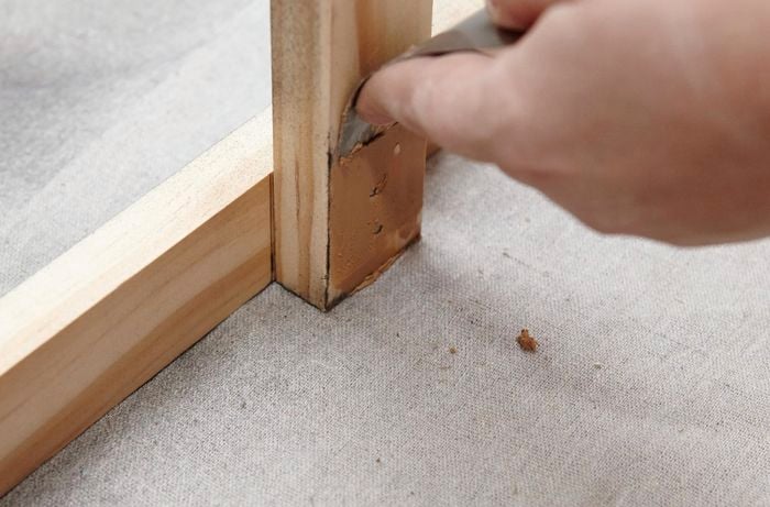 Person using wood filler on bit of timber to cover up major holes.