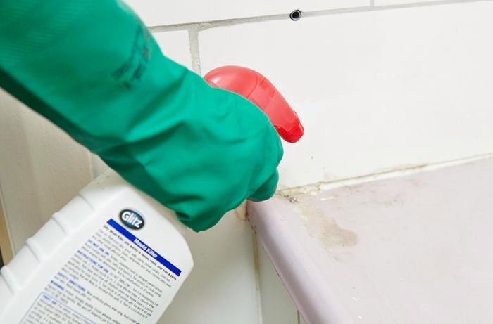 A person wearing rubber gloves spraying a line of grout using a spray bottle