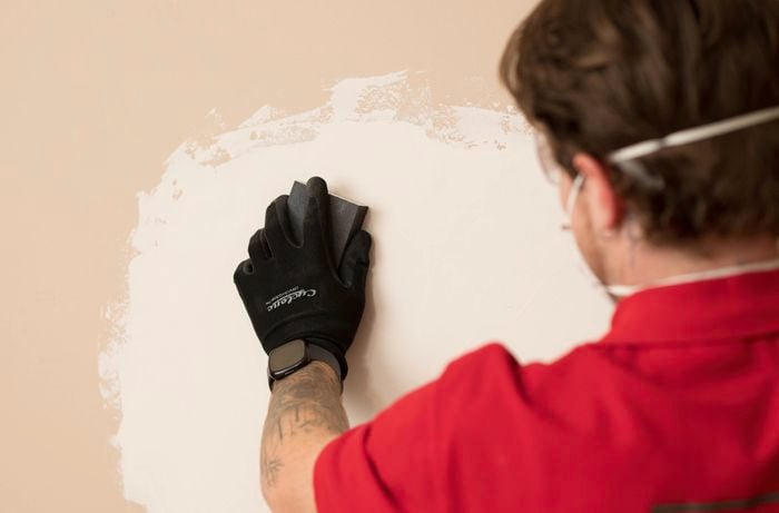 A gloved hand is using a sanding block to smooth out any bumps on the wall.