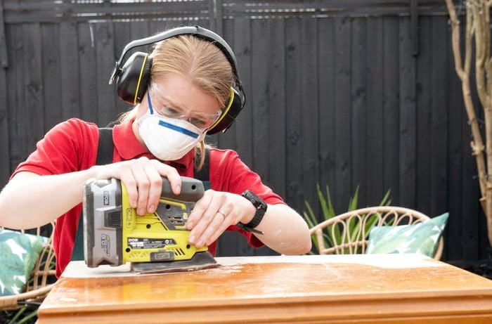 Woman using cordless sander to sand a pine chest
