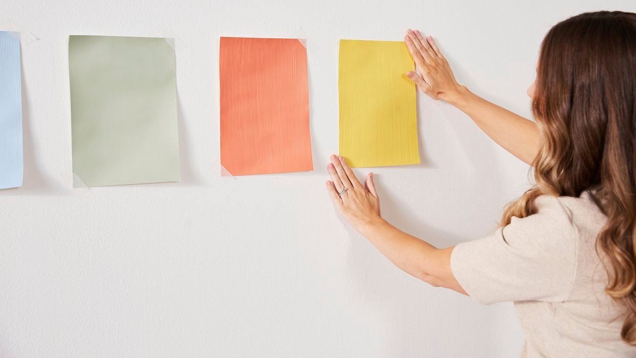 A woman hanging paint swatches on a white wall