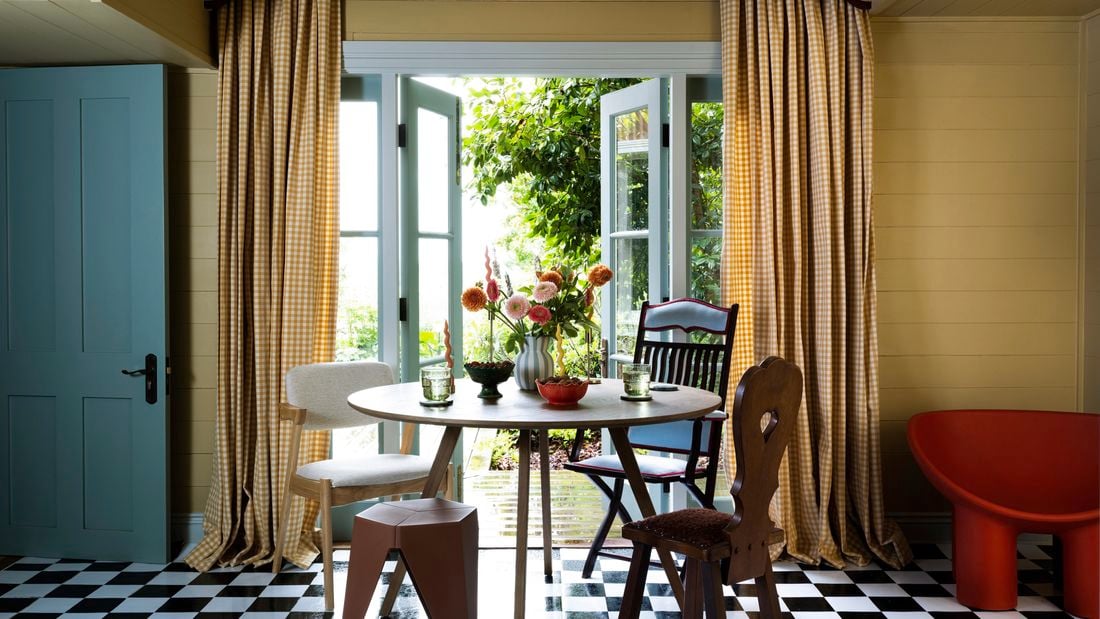 Dining setting with chairs, drapery, checked floors and opened doors leading outside.